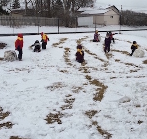 kids rolling snowballs in the school yard
